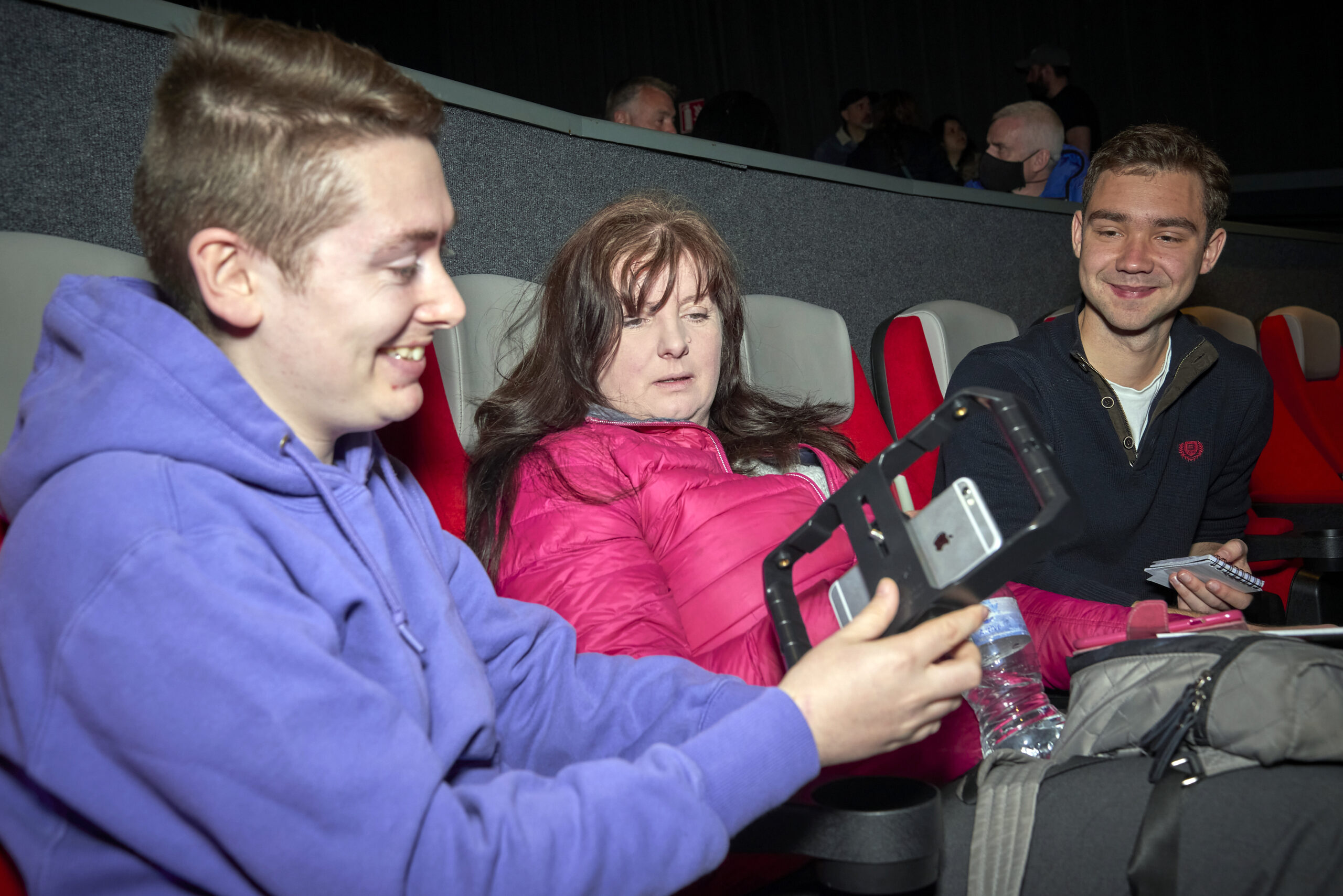 Three people seating in cinema seats smiling holding phones